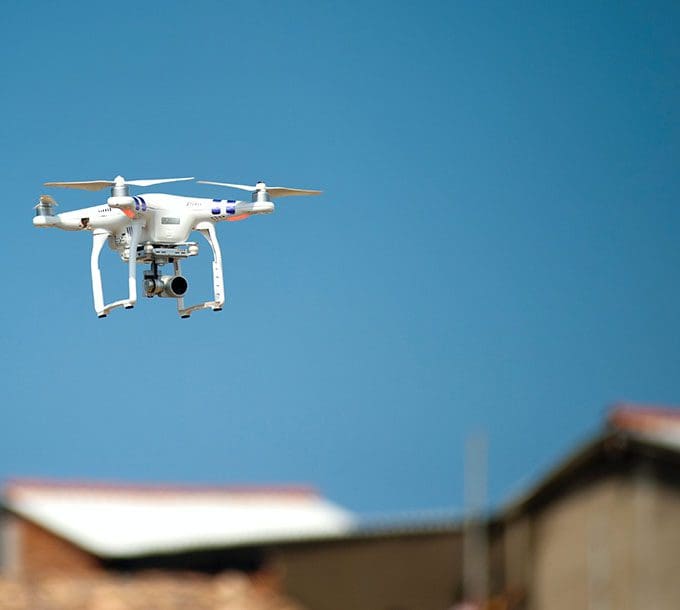 A white drone flying in the air over some buildings.