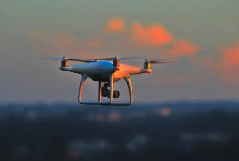 A white and blue drone flying in the sky.