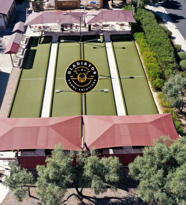 Aerial view of a sports complex featuring four pickleball courts marked with the gladiator logo, surrounded by red canopies and greenery.