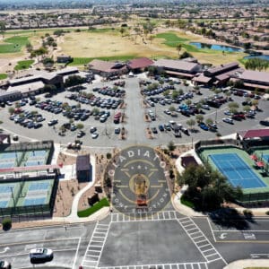 Aerial view of a large parking lot at a sports complex featuring tennis courts and golf courses, with surrounding residential areas.