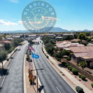 Aerial view of a residential street with single-story houses and an american flag, under a clear sky with a watermark at the top center.