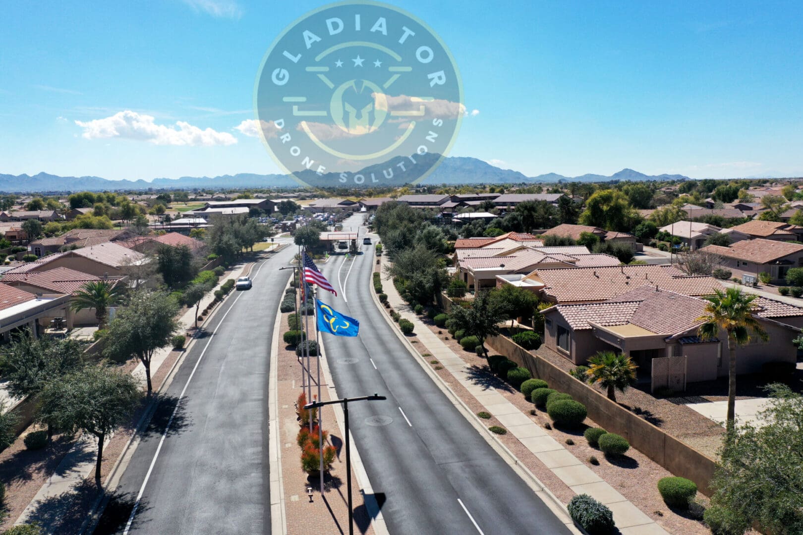 Aerial view of a residential street with single-story houses and an american flag, under a clear sky with a watermark at the top center.