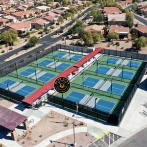 Aerial view of a community park with multiple pickleball courts, each marked by a red logo at the center, surrounded by residential houses.