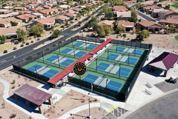 Aerial view of a community park with multiple pickleball courts, each marked by a red logo at the center, surrounded by residential houses.