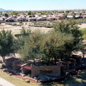 Aerial view of trilogy residential community entrance with lush greenery and surrounding houses.