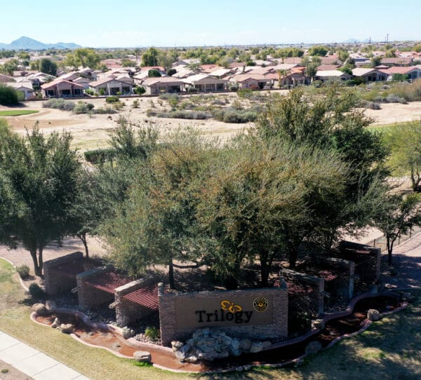 Aerial view of trilogy residential community entrance with lush greenery and surrounding houses.