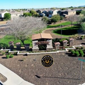 Aerial view of a suburban entrance sign reading "victoria" with surrounding neatly manicured lawns and residential homes, set against a mountain backdrop.