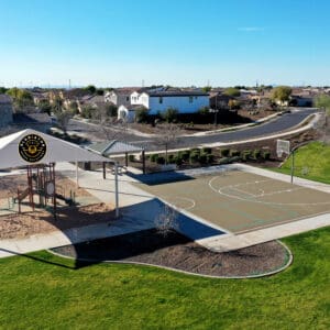 Aerial view of a community park with a covered playground, basketball court, and surrounding residential area.