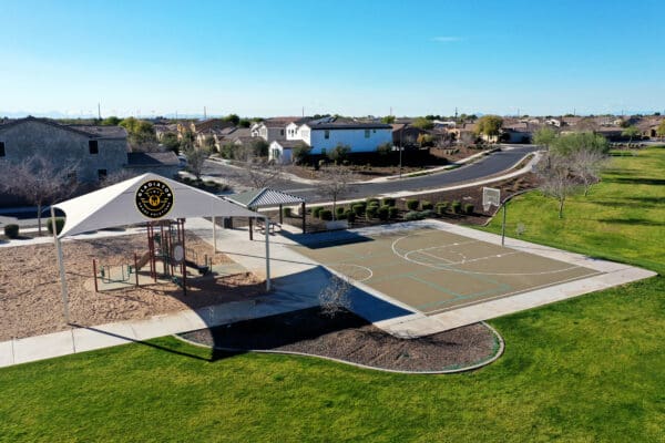 Aerial view of a community park with a covered playground, basketball court, and surrounding residential area.