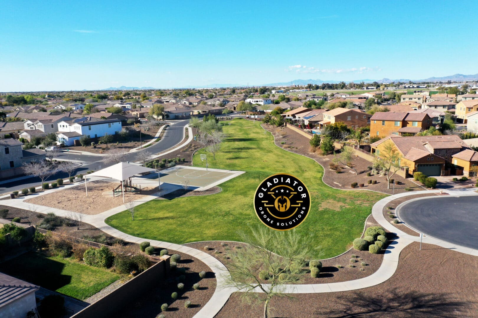 Aerial view of a suburban neighborhood with houses, roads, and a park, under a clear blue sky. a watermark with a logo is visible at the center.