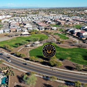 Aerial view of a suburban neighborhood with houses, roads, and a golf course, marked by a circular logo in the center.