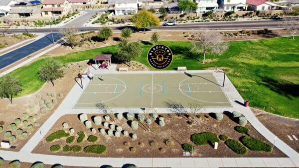 Aerial view of a basketball court in a suburban park with people playing and nearby residential houses.