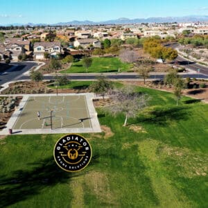 Aerial view of a suburban neighborhood featuring a basketball court and park, with houses and mountainous background.