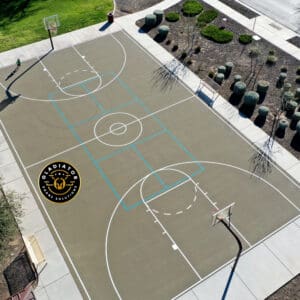 Aerial view of an outdoor basketball court with distinctive markings and a logo at the center, surrounded by landscaping and trees.