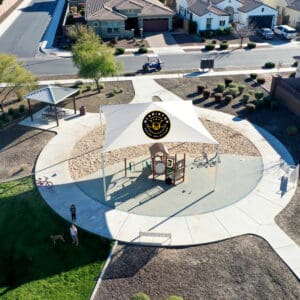 Aerial view of a suburban park with a circular playground, basketball court, and walking paths, surrounded by residential houses.